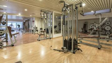 A gym with various exercise equipment, wooden floors, and mirrored walls.