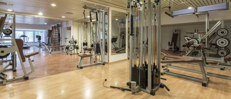 A gym with various exercise equipment, wooden floors, and mirrored walls.