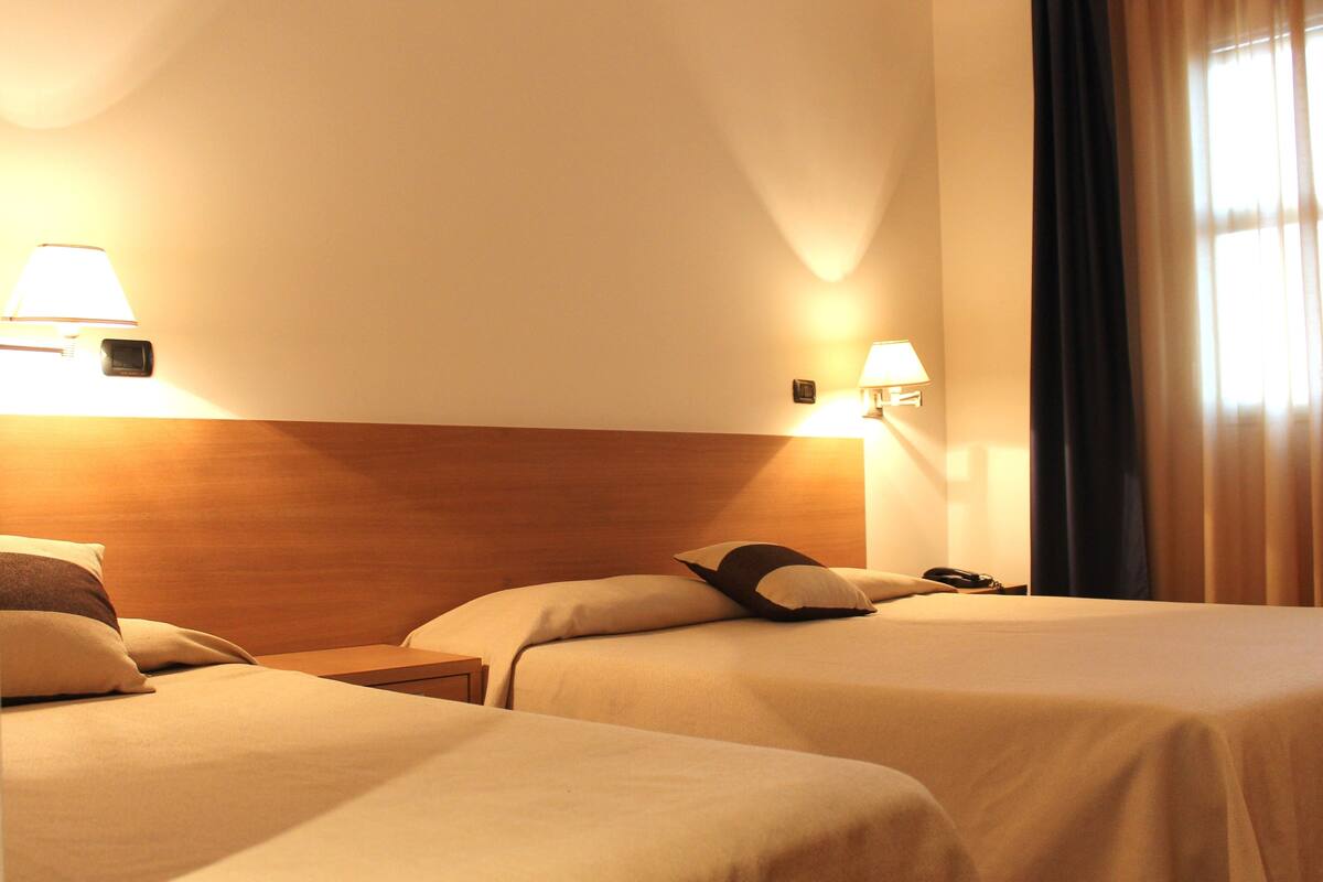 Une chambre d’hôtel avec deux lits, chacun étant équipé d’un oreiller et d’une table de chevet. Des lampes murales sont fixées de chaque côté des lits.