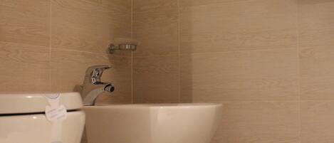 A bathroom with a white toilet and sink, beige tiled walls, and a silver faucet.