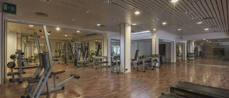 Une salle de sport dotée d’un plancher en bois, de divers appareils d’exercice et d’un mur recouvert de miroirs.