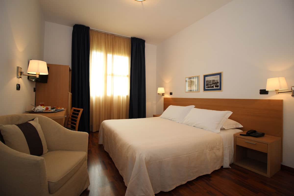 Une chambre d’hôtel avec un lit, une chaise, un bureau et une table de chevet.