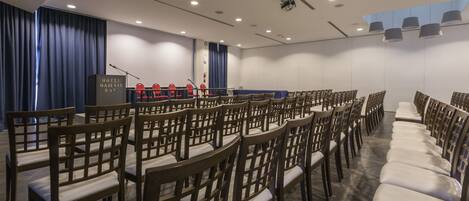 A conference room with rows of wooden chairs and a podium at the front.