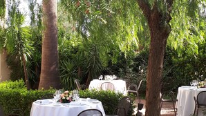 Un área de comedor al aire libre con mesas redondas preparadas para una comida, rodeada de exuberante follaje y árboles.