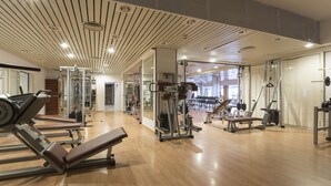 Un gimnasio moderno con suelo de madera, diversos equipos de ejercicio y grandes espejos.