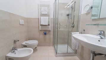 Un baño moderno con bidé, ducha con mampara de vidrio y un lavamanos grande.