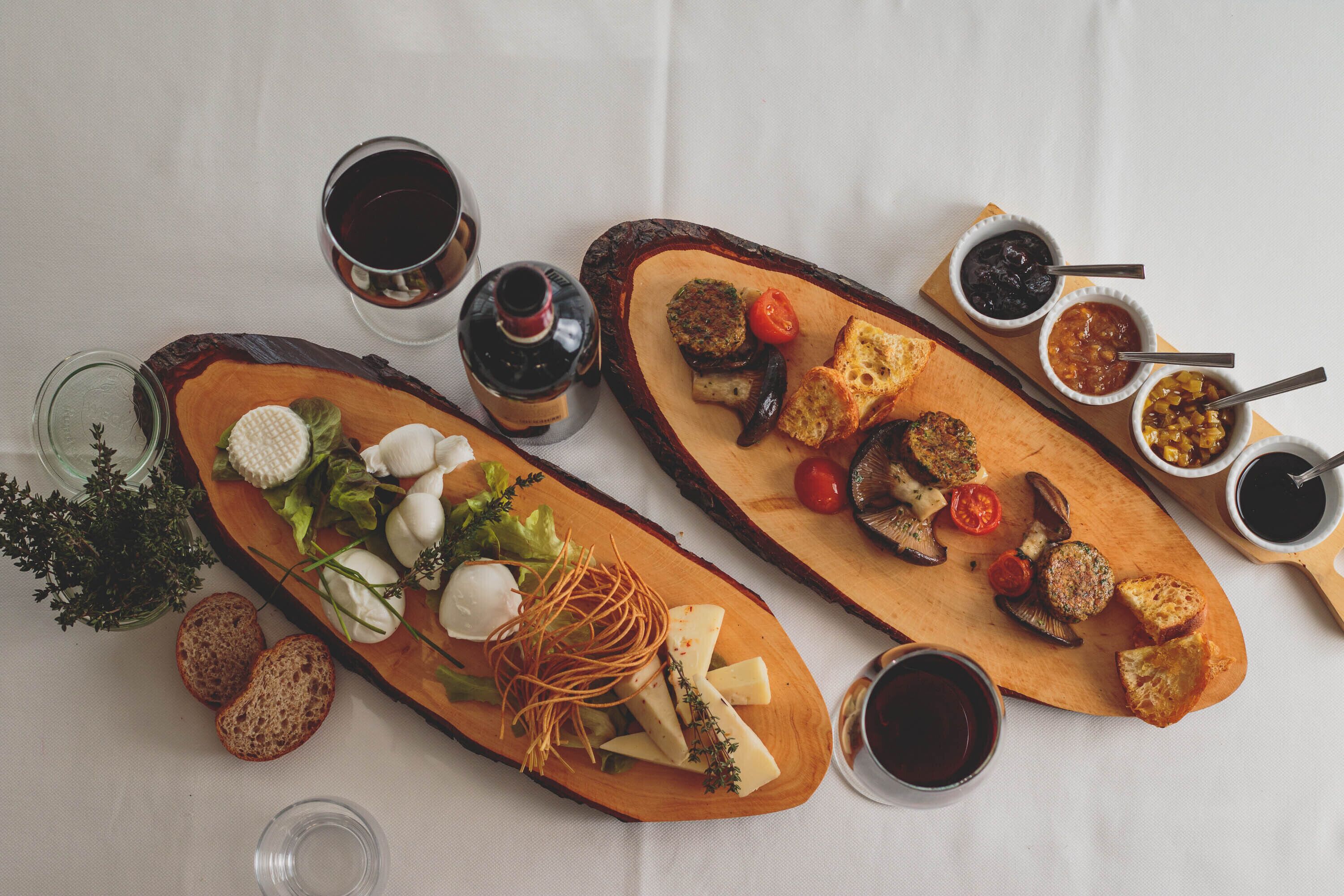 En træplanke med forskellige oste, grøntsager og brød, samt små skåle med saucer og et glas vin.