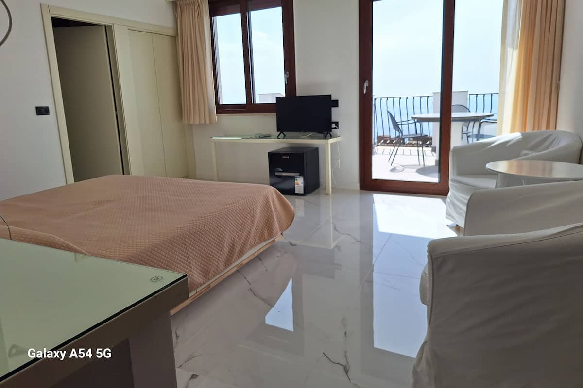 A hotel room with a bed, a TV, a desk, a chair, and a balcony with a table and chairs.