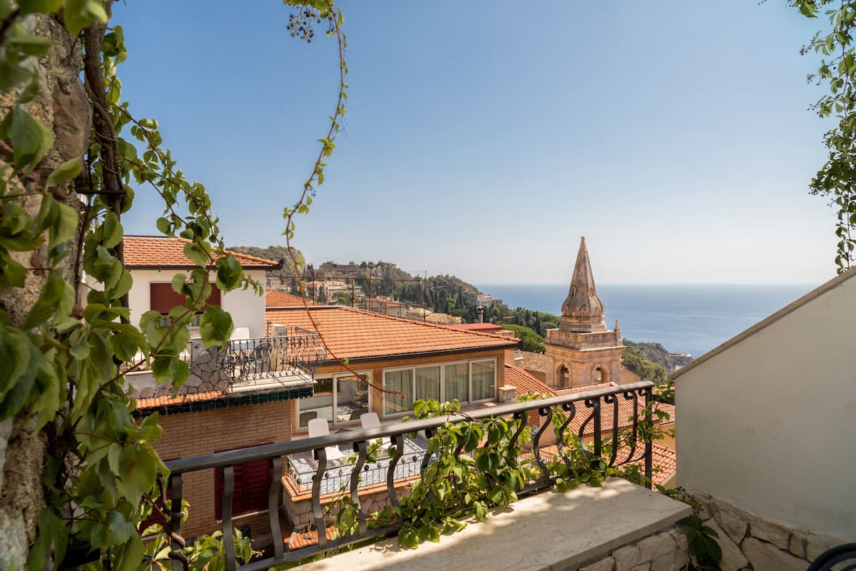 A balcony with a view of a coastal town, including a church tower and a building with a tiled roof.