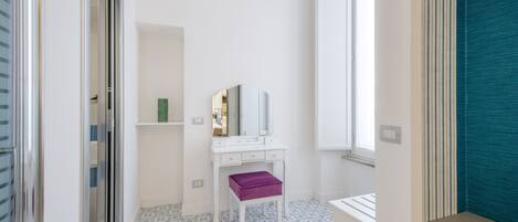 A bathroom with a white vanity, a purple stool, a mirror, and patterned floor tiles.