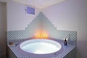 Un baño con una bañera independiente, un ventanal pequeño y un diseño decorativo en la pared.