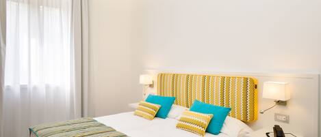 A hotel room with a bed, two bedside lamps, a telephone, and a window with curtains.