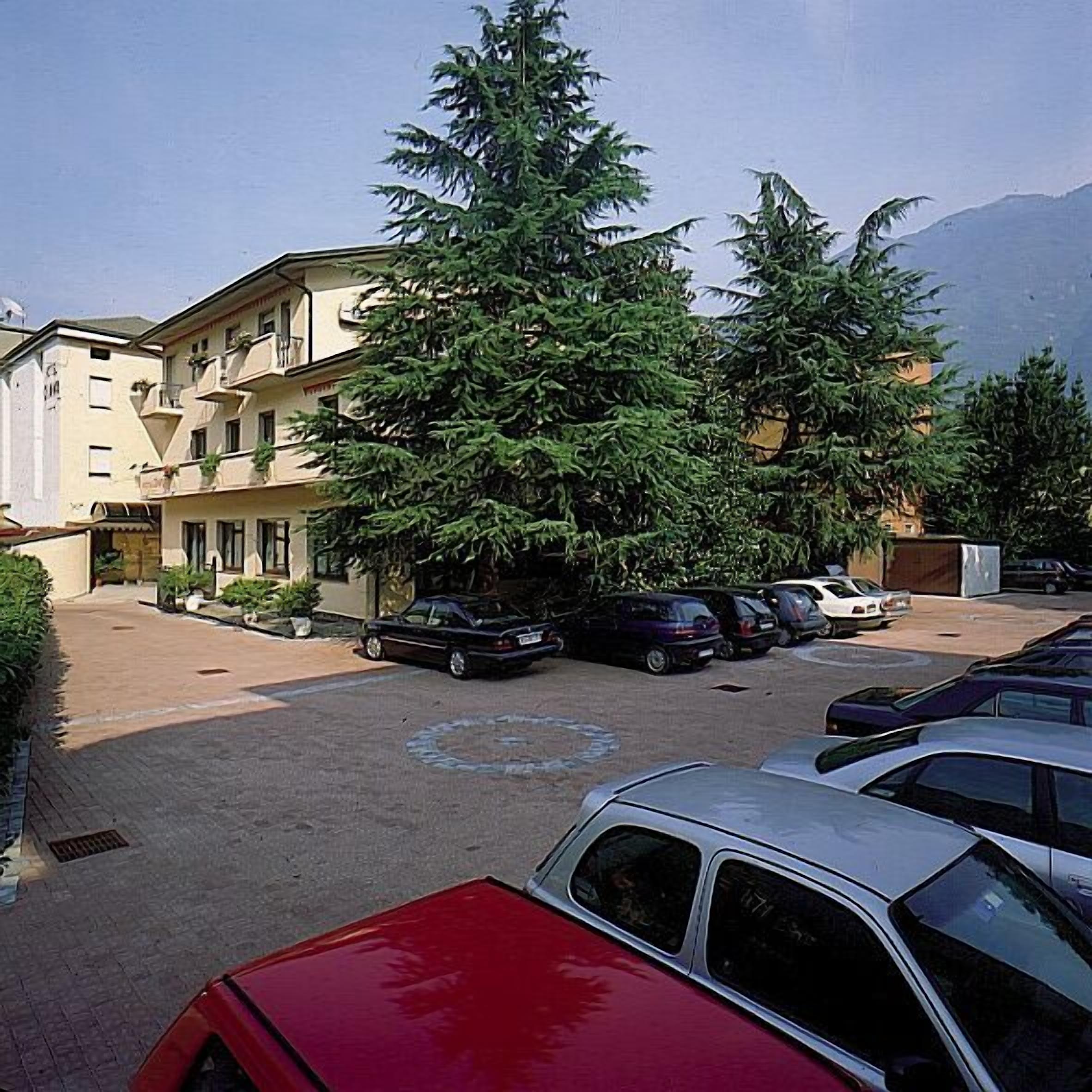 Un estacionamiento con varios coches, un árbol grande y un edificio con múltiples balcones.
