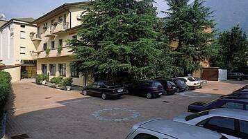Un estacionamiento con varios coches, un árbol grande y un edificio con múltiples balcones.
