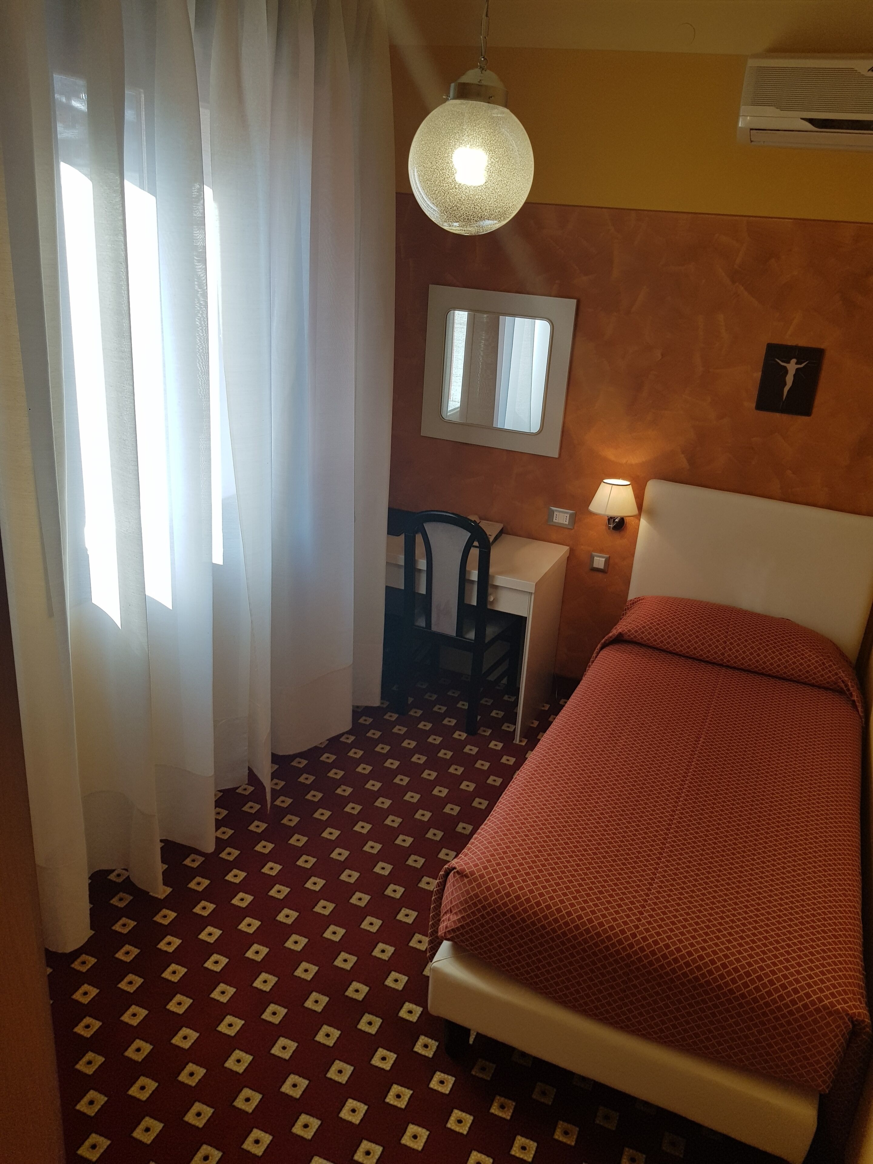 Ein Hotelzimmer mit Bett, Schreibtisch, Stuhl, Spiegel und einer Pendelleuchte.