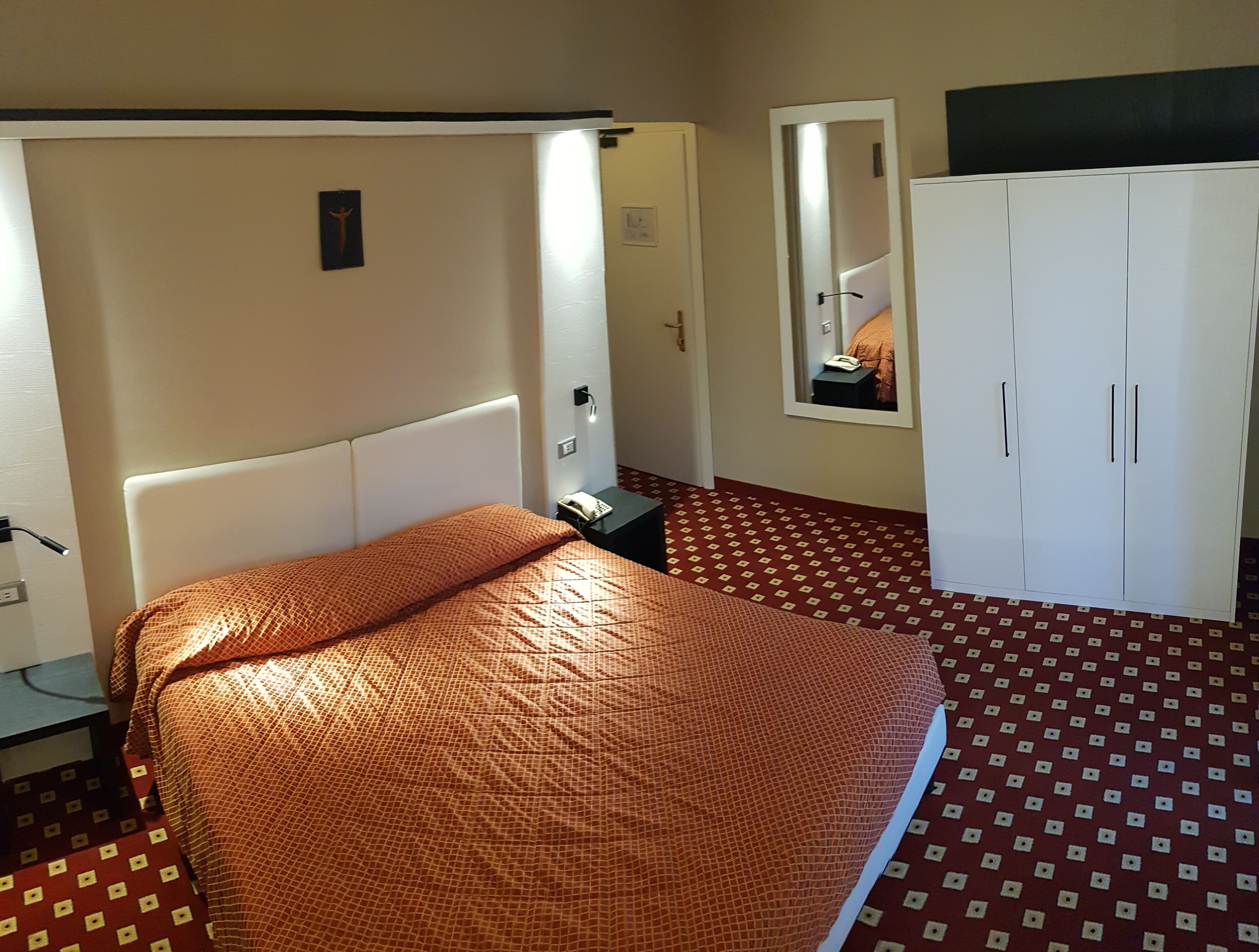 Une chambre d’hôtel avec un lit, une armoire, un miroir et un téléphone sur une table de chevet.