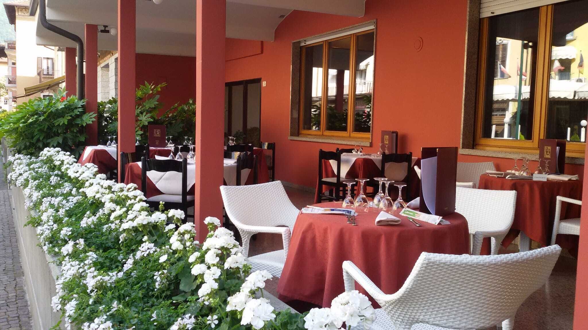 An outdoor cafe with tables and chairs, surrounded by white flowers and a red building facade.