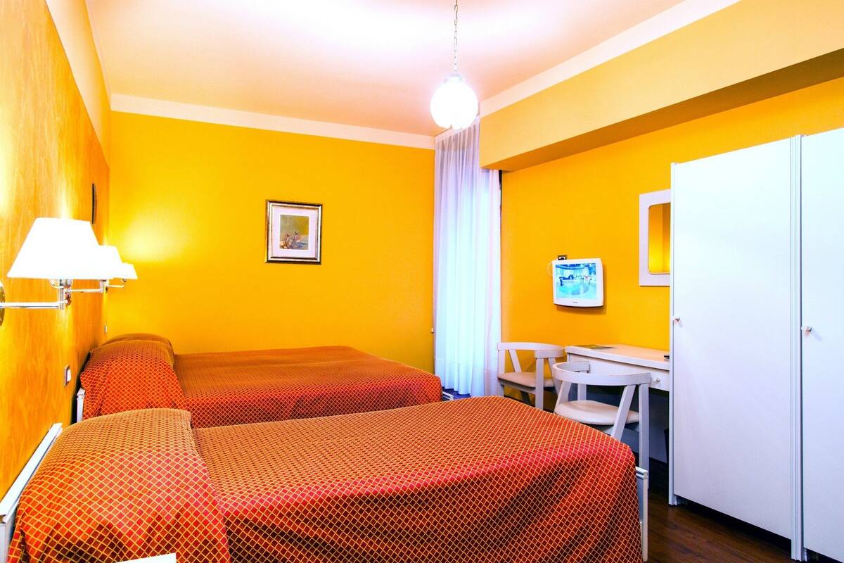 Une chambre avec deux lits, un bureau, une chaise, une lampe et une porte.
