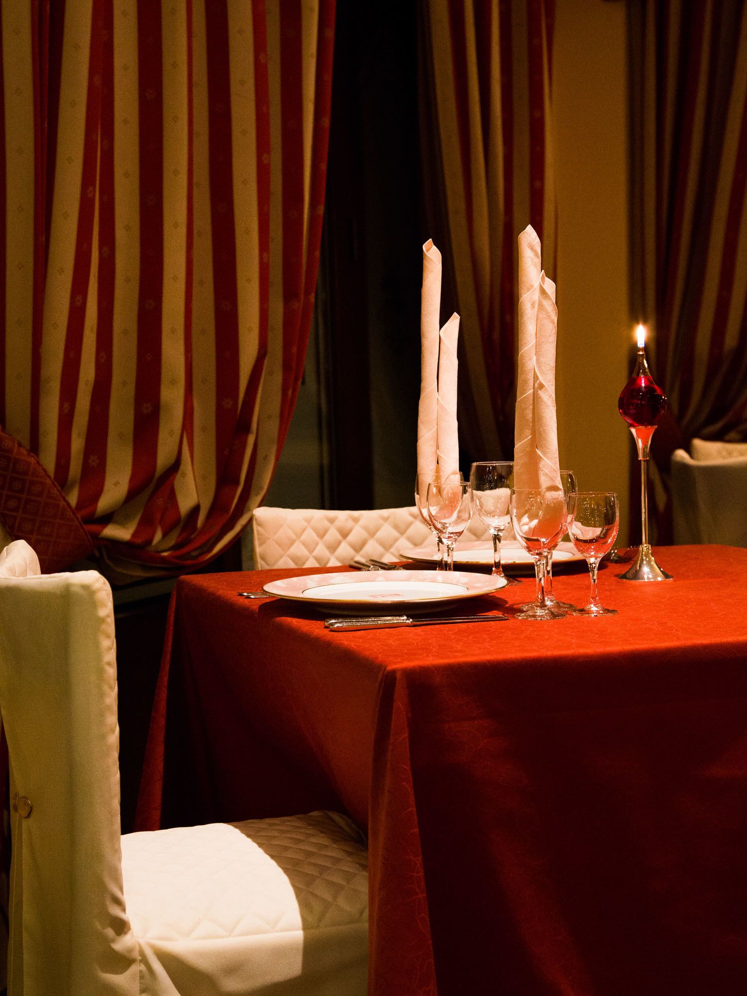 Tavola imbandita per la cena, con tovaglia rossa, tovaglioli bianchi e bicchieri da vino.