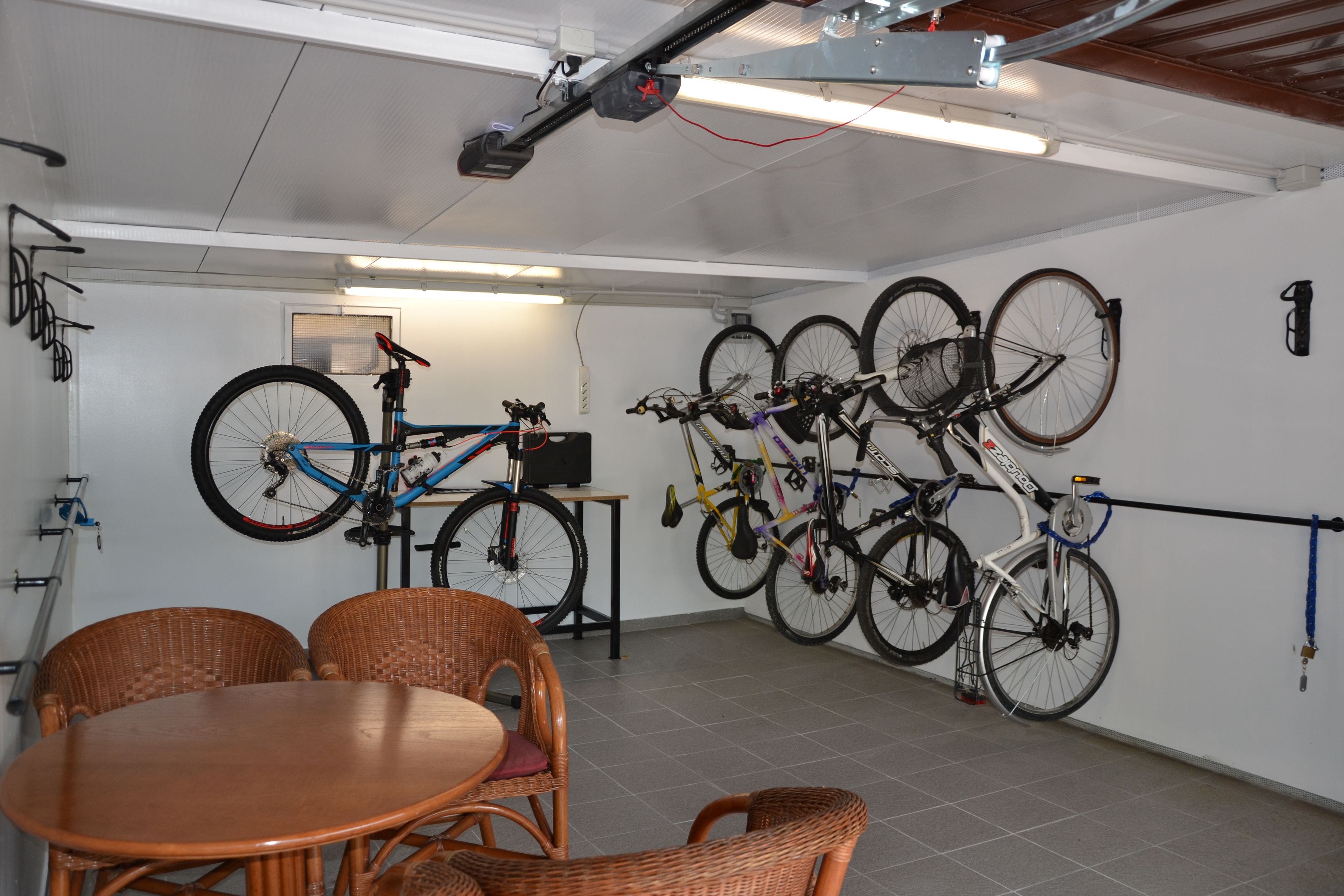 A room with a dining table and chairs, a ceiling-mounted projector, and multiple bicycles mounted on the wall.