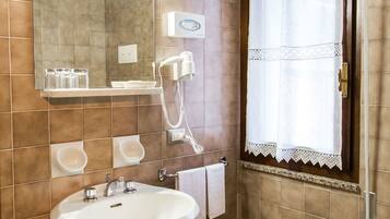 Un baño con lavamanos pedestal, espejo sobre tocador, ventana con cortina y bidé.