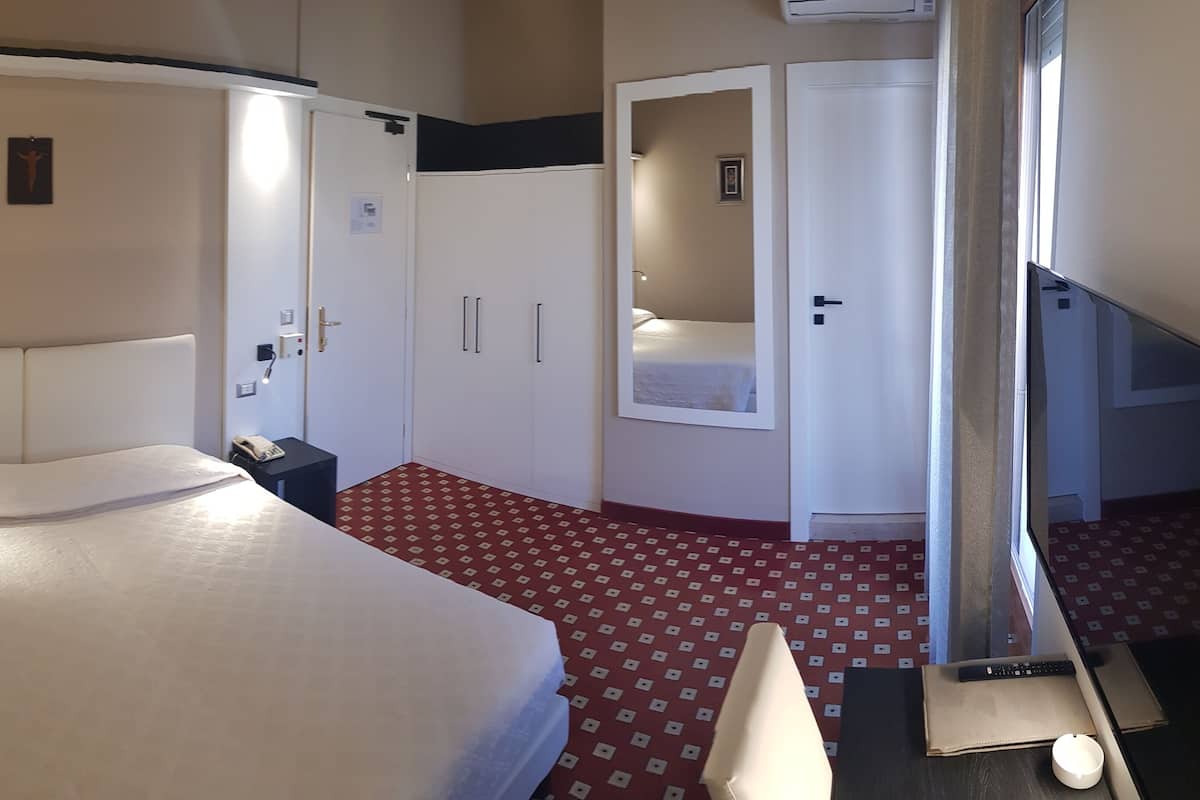 Une chambre d’hôtel avec un lit, une armoire, un bureau et un miroir.