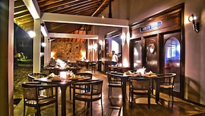 An outdoor dining area with wooden tables and chairs, a stone wall, and a sign reading "City Shark". - Weligama Bay Resort (Weligama)