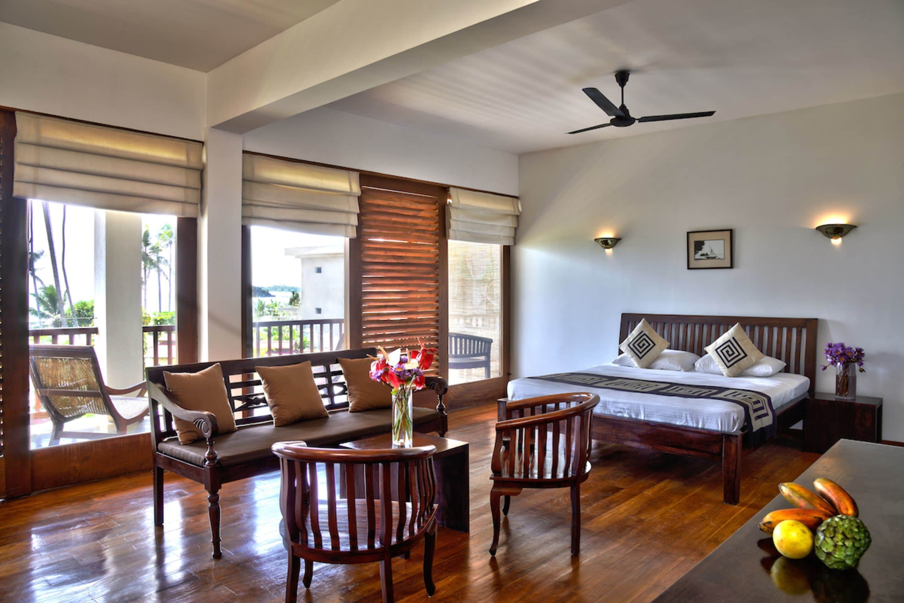 A well-lit bedroom with a bed, bedside tables, and a seating area with chairs and a sofa.