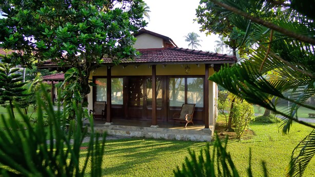 A house with a covered porch, a lawn, and surrounding greenery. - Weligama Bay Resort (Weligama)