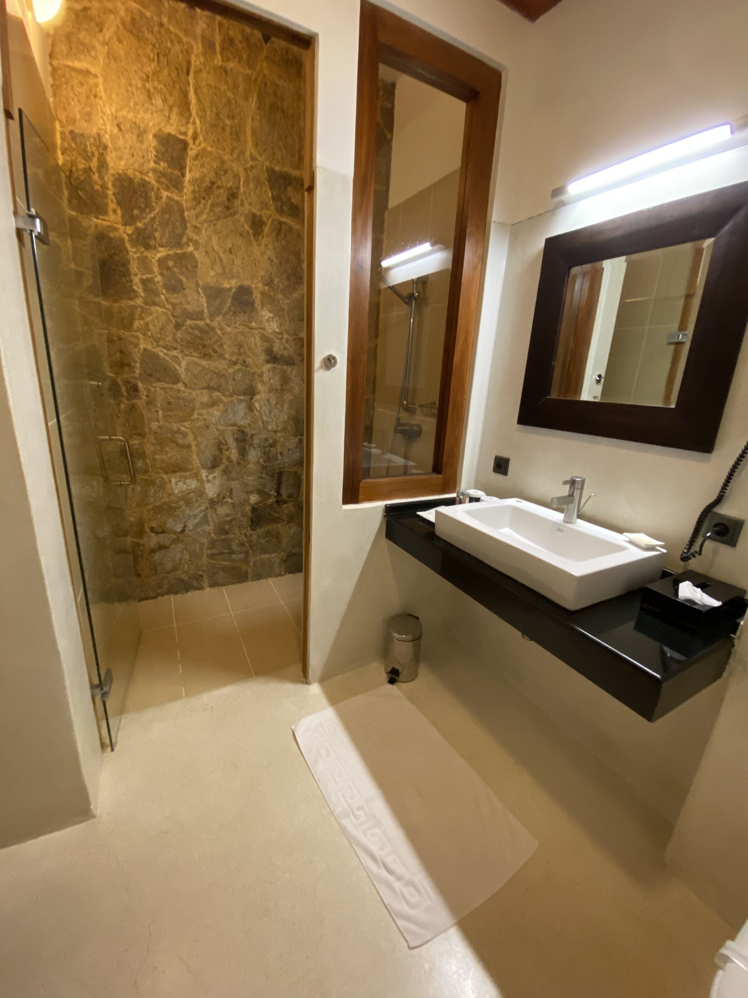 A bathroom with a stone wall, a glass shower enclosure, a white sink, and a mirror.