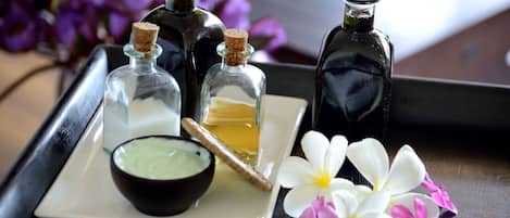 A tray with three glass bottles, a bowl of green substance, a wooden stick, and two flowers.