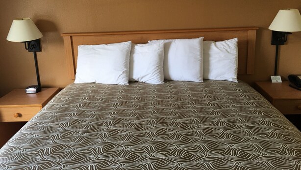Une chambre d’hôtel comprenant un lit, deux lampes de chevet, un téléphone sur la table de chevet et une lampe fixée au mur.