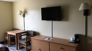 Une chambre d’hôtel équipée d’un bureau, de deux chaises, d’une commode, d’un téléviseur et de deux lampes fixées au mur.