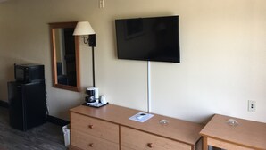 Une chambre d’hôtel avec une commode en bois, un téléviseur à écran plat fixé au mur, une lampe et un four à micro-ondes posé sur une petite table.