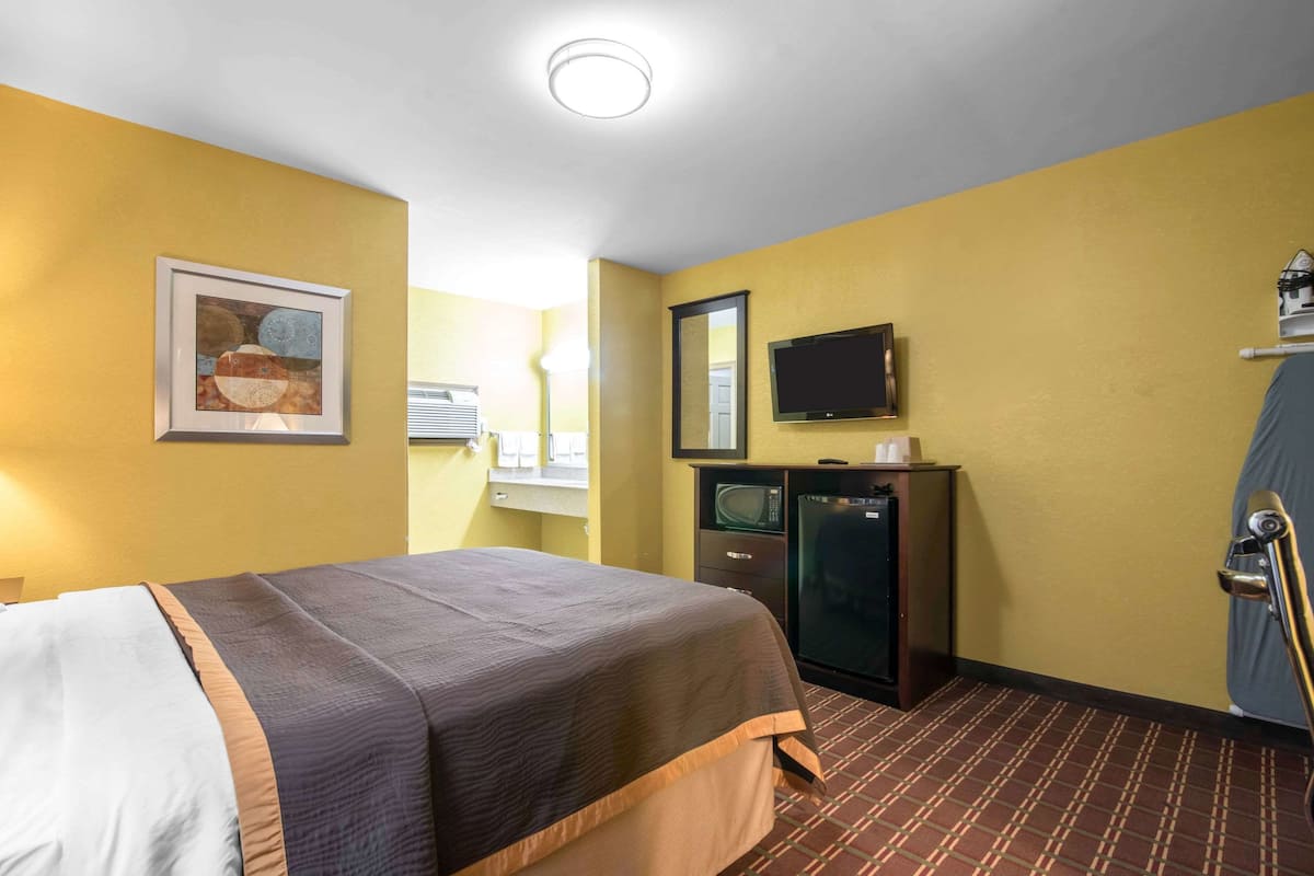 Habitación de hotel con cama, televisor, microondas y ventana con persianas.