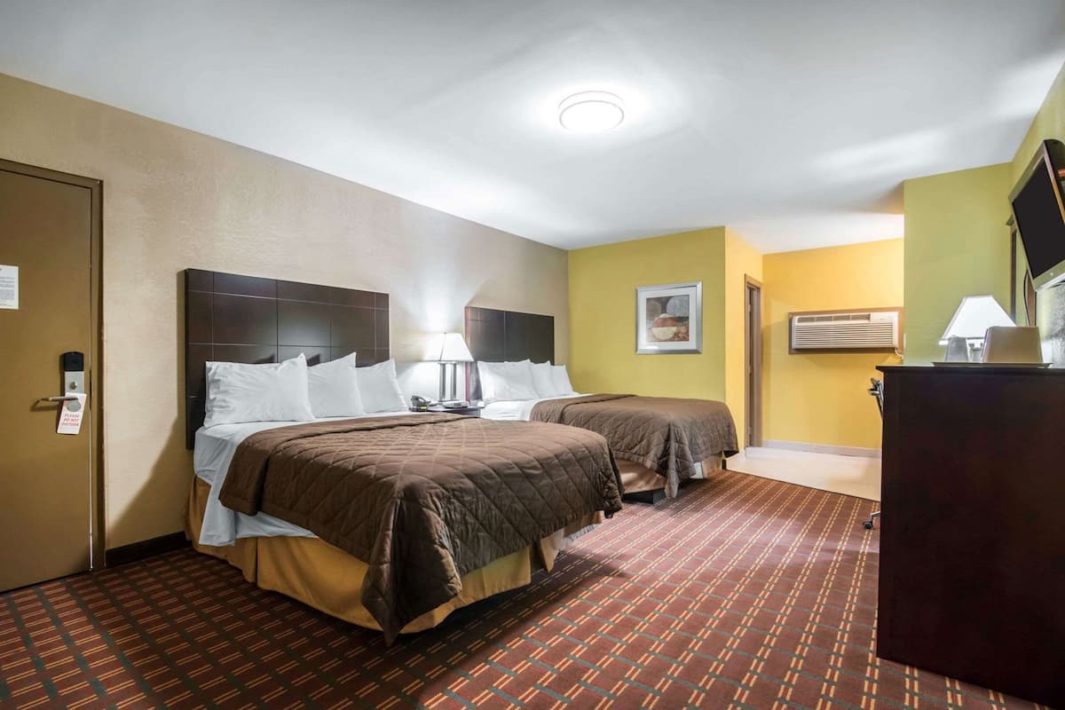 Habitación de hotel con dos camas, un escritorio, una silla, una lámpara y un televisor.