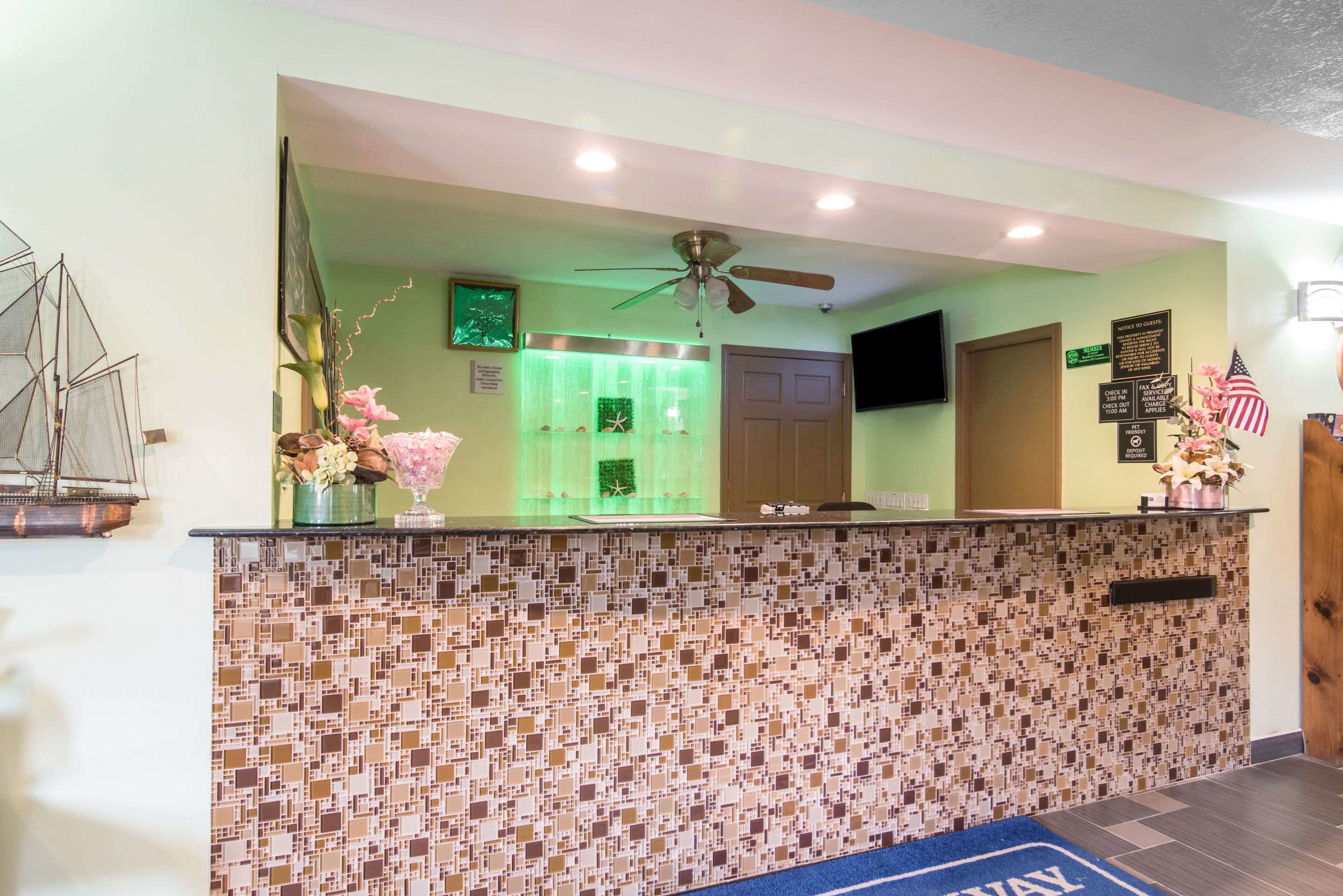 A reception area with a mosaic tile wall, a ceiling fan, and a blue carpet with "WELCOME" text.