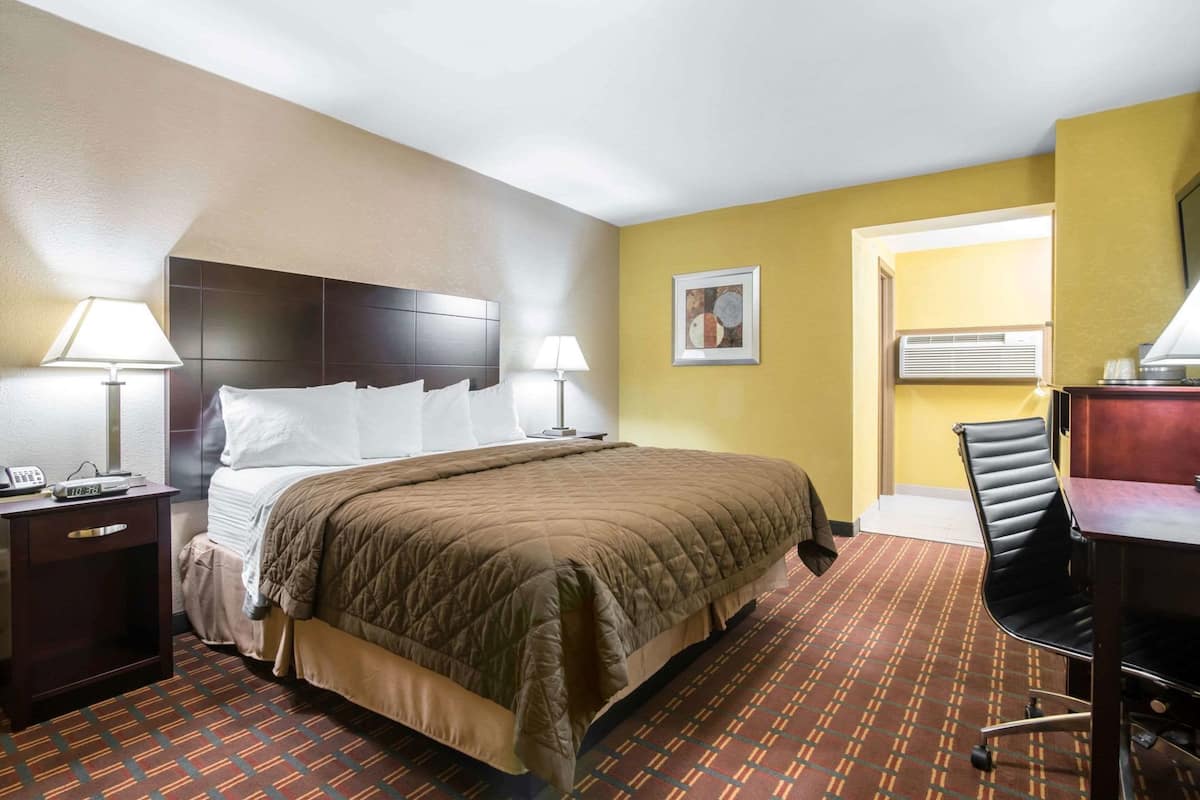 Habitación de hotel con cama, lámparas de noche, escritorio con silla y aire acondicionado instalado en la pared.