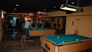 A pool hall with two pool tables, a bar area, and a Budweiser sign.