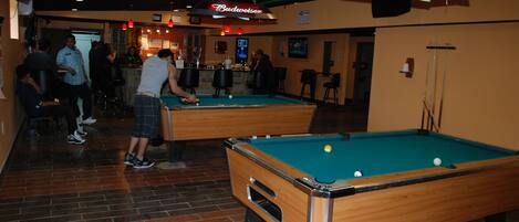 A pool hall with two pool tables, a bar area, and a Budweiser sign.