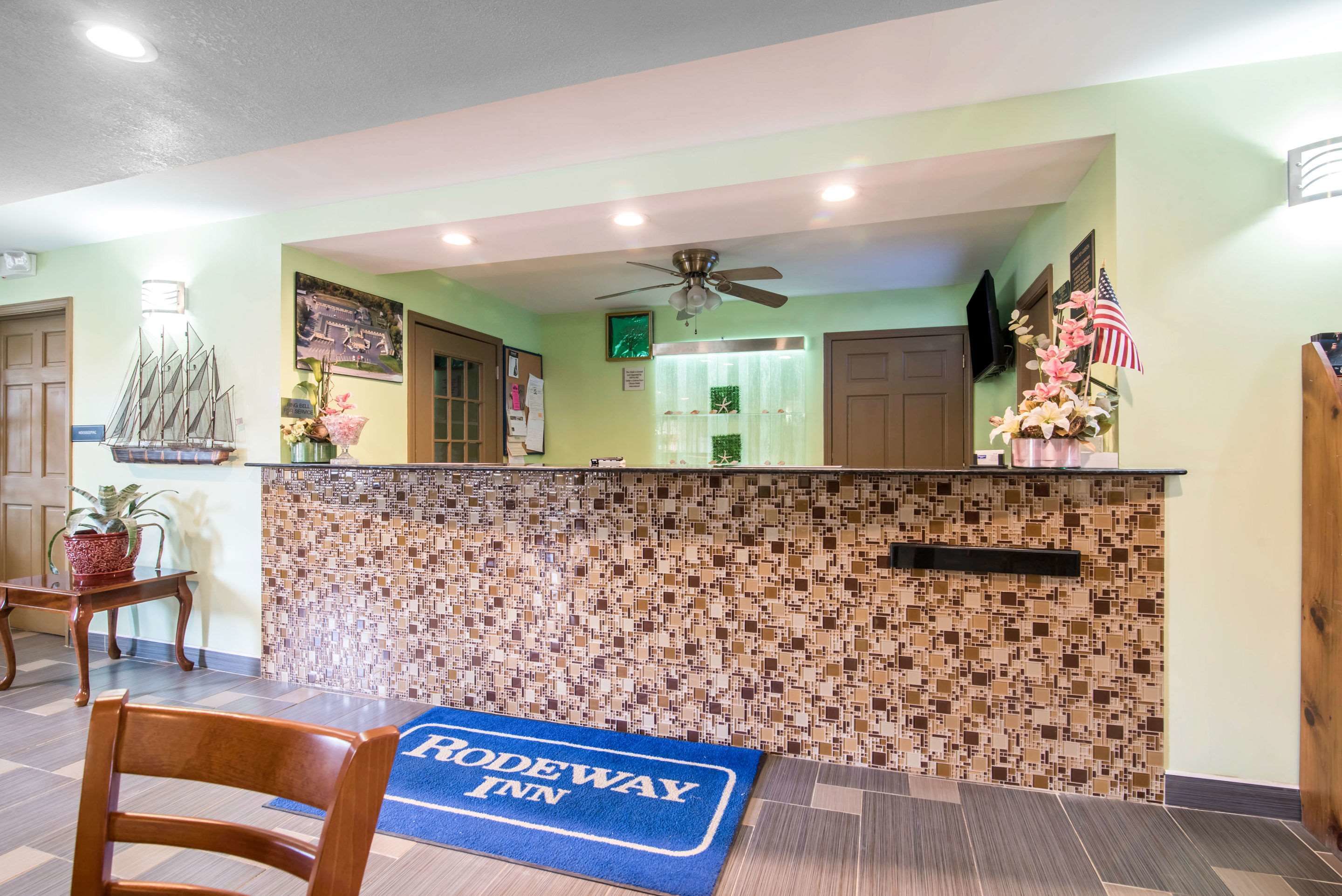 A reception area with a tiled wall, a blue mat with "Rodeway Inn" text, a wooden chair, and a ship decoration.