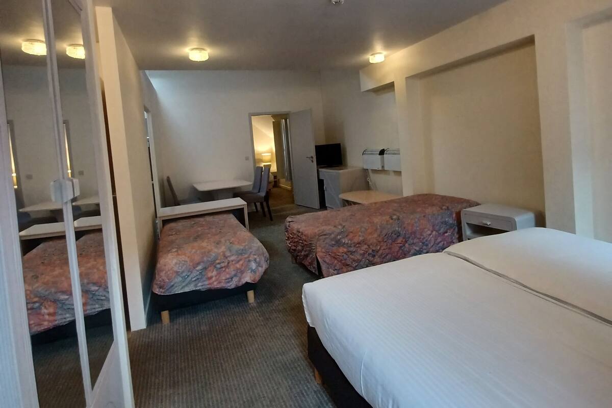 Une chambre d’hôtel avec deux lits, un bureau, une chaise, une télévision et une petite kitchenette.