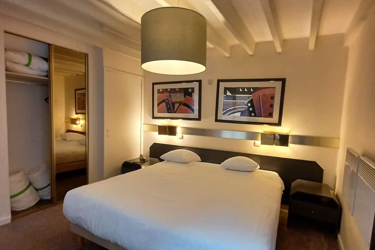 Une chambre d’hôtel avec un grand lit, une armoire, une table de chevet et une lampe.