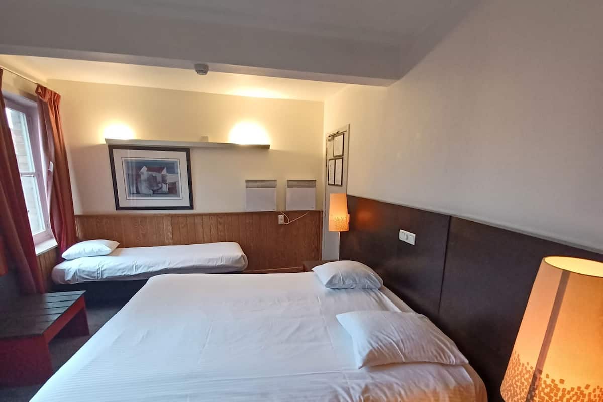 Une chambre d’hôtel avec deux lits, un bureau, une lampe et un tableau encadré au mur.