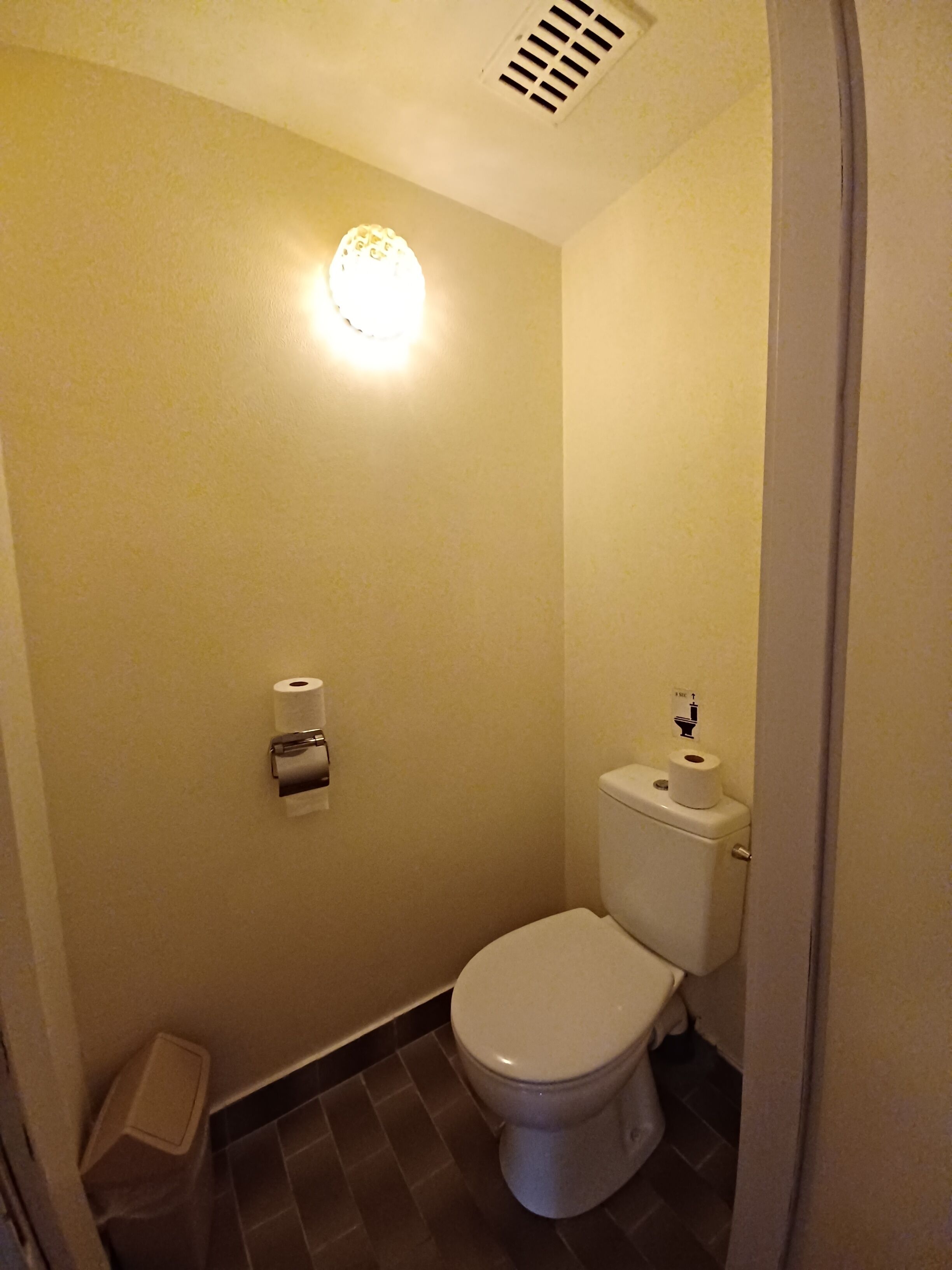 A small, compact bathroom with a toilet, a hand dryer, and a paper towel dispenser.