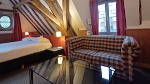 Een kamer met een hoogslaper, een geruit bankje, een glazen tafel en een raam met gordijnen.