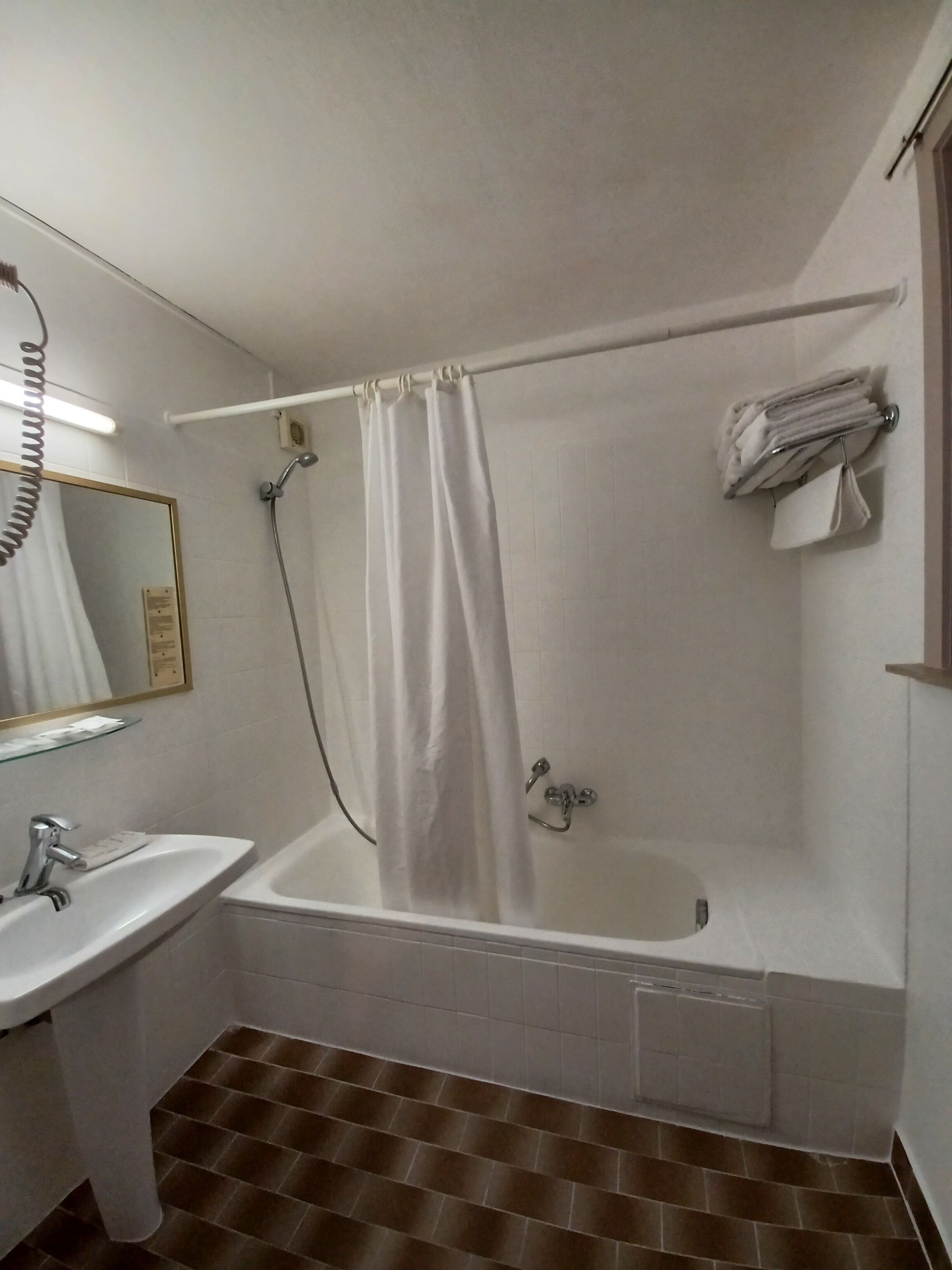 Un baño con bañera, lavamanos, espejo y toallero.
