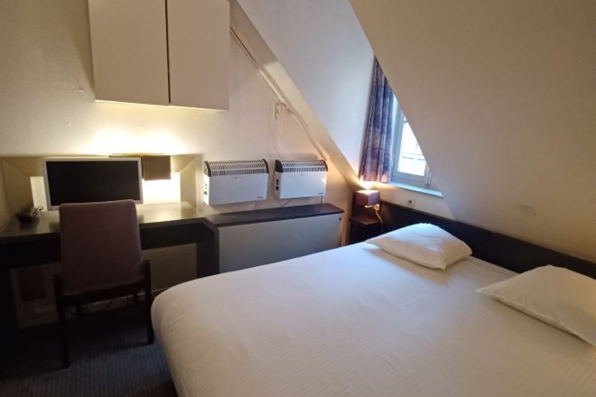 Een hotelkamer met een bed, bureau, stoel en twee wandairconditioners.