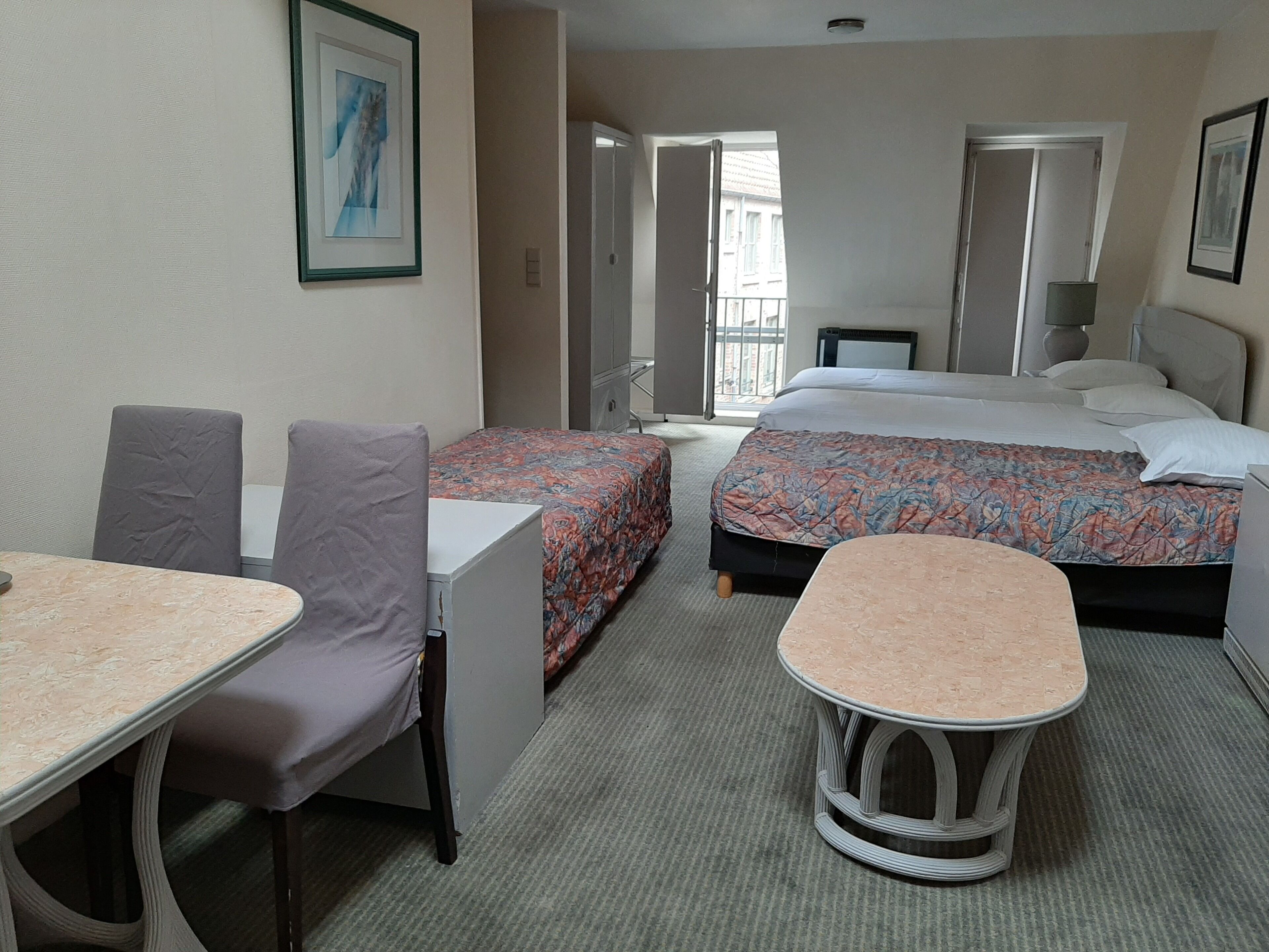 A hotel room with a bed, a desk, two chairs, a small table, and a door leading to a balcony.