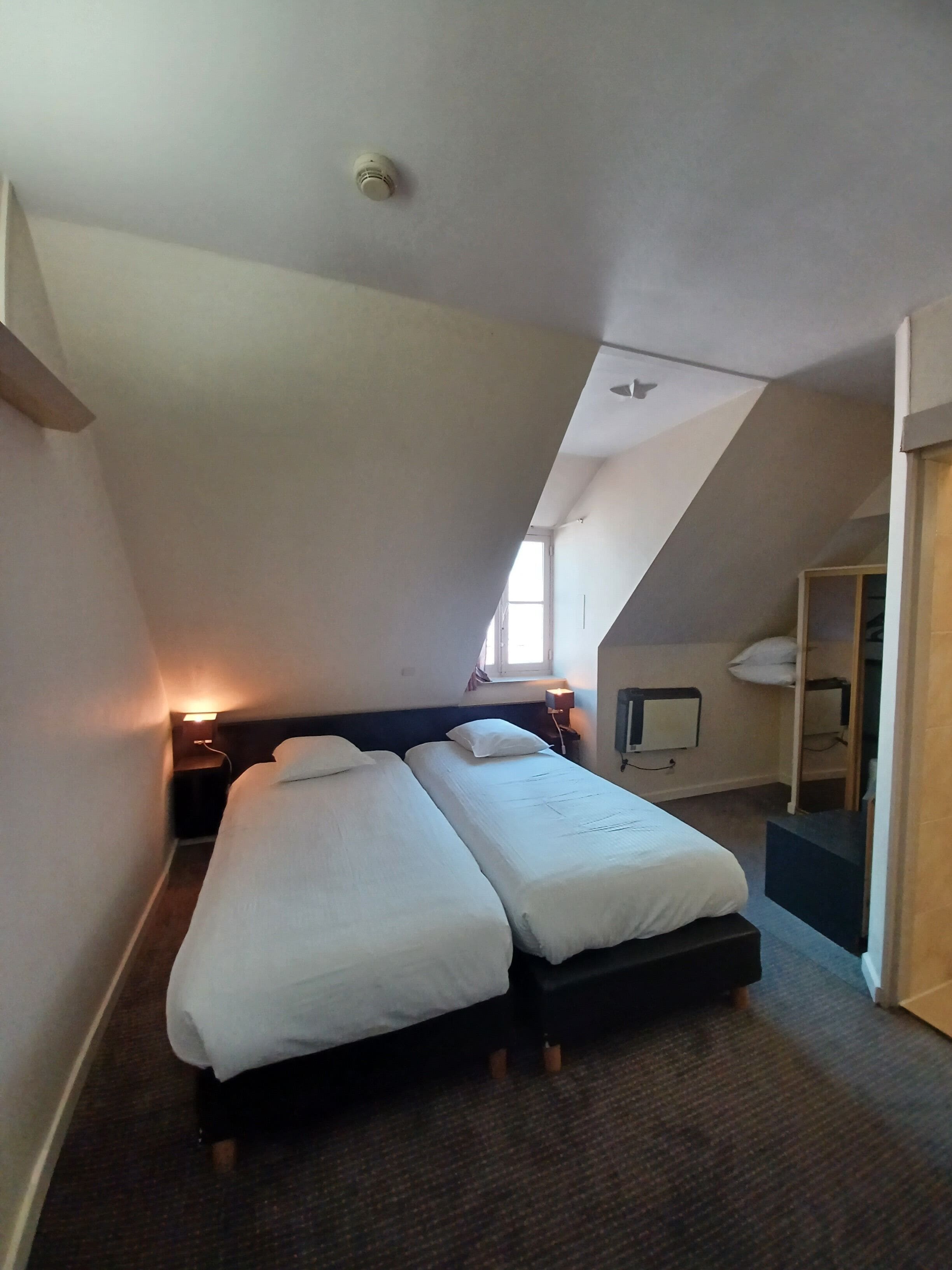 Habitación de hotel con dos camas, una ventana, un escritorio y un espejo.